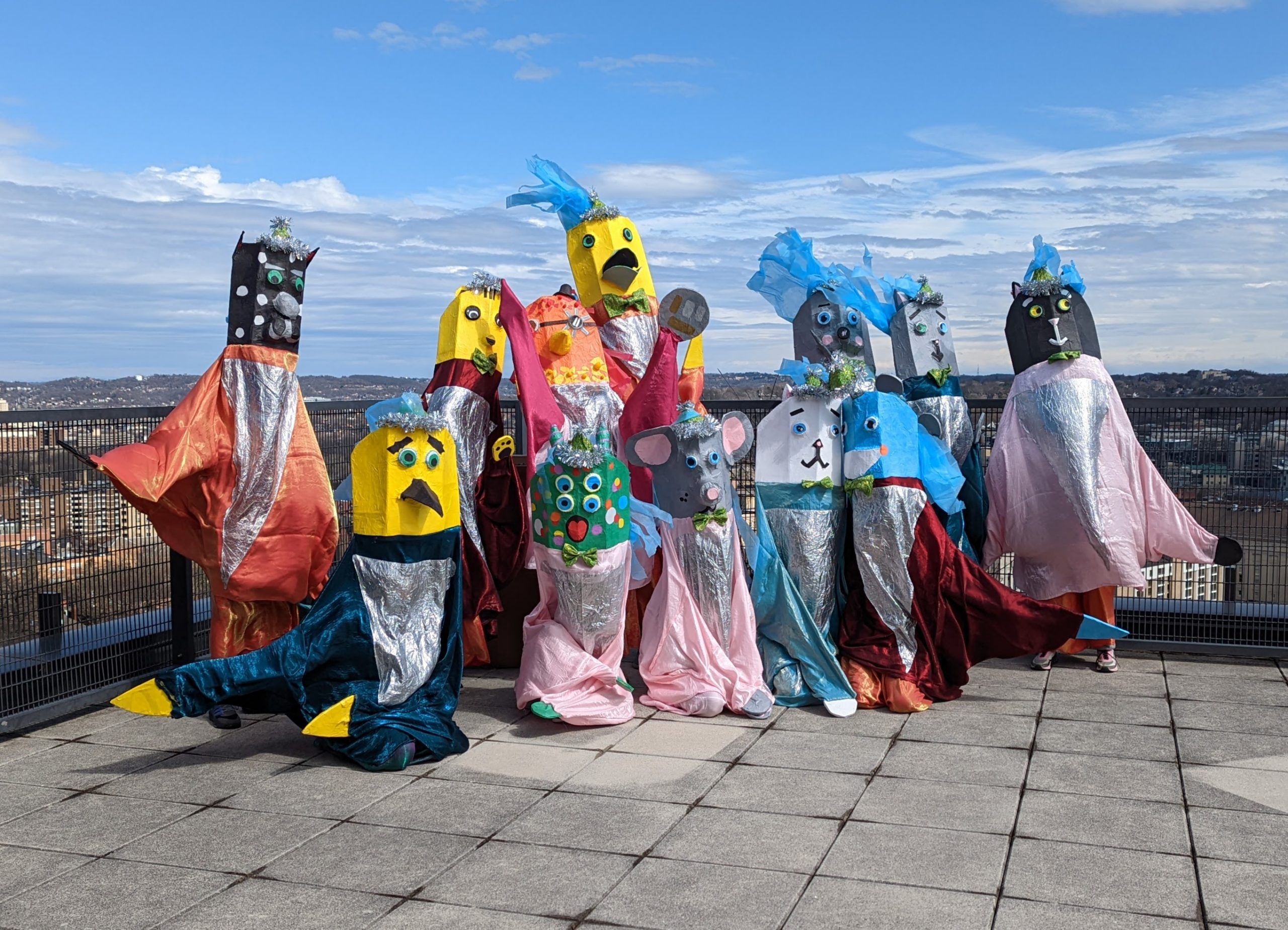 Colorful giant puppets pose for a picture on a rooftop with a bright blue sky background.